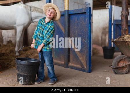 Boy lugging bucket in stable Stock Photo