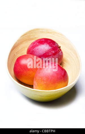 Close-up of fresh mangoes in a bamboo bowl on white background Stock Photo