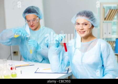Confident clinician studying new substance in laboratory with her colleague on background Stock Photo