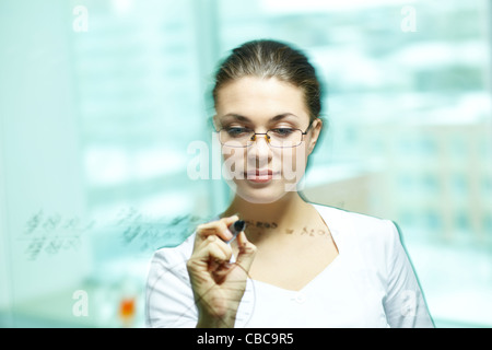 Young chemist looking at board while writing on it Stock Photo
