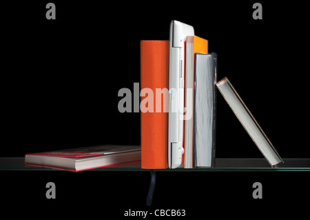 white laptop computer between books on the glass shelf Stock Photo