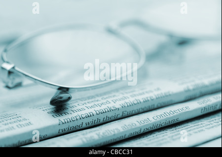 Eyeglasses lie on a pile of newspapers.Blue toned. A photo close up. Selective focus Stock Photo