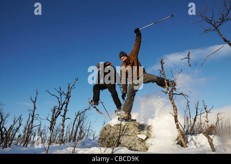 Skiers jumping off rock in snow Stock Photo