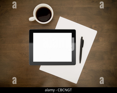 Contemporary digital tablet with blank screen lying on worktable with paper, pen and cup of coffee. Top directly above view. Stock Photo