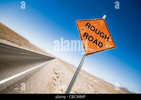 Weathered orange Rough Road warning sign near a tarmac road in Death Valley Stock Photo