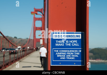 A sign on Golden Gate Bridge detailing Crisis Counseling, the sign reads There is hope make the call, a man is walking away Stock Photo