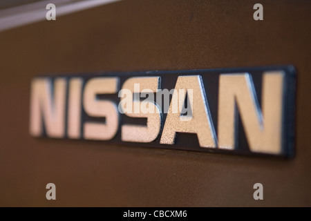 Detailed view of a rusted chrome Nissan name plate on a brown 1984 pickup truck. Stock Photo