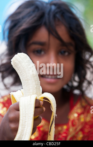 Happy young poor lower caste Indian street girl eating a banana. Andhra Pradesh, India. Selective focus. Stock Photo