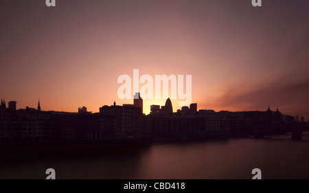Sun rising over urban buildings on river Stock Photo