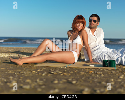happy, young couple, dressed in white, relaxing, having a picnic by the sea shore Stock Photo