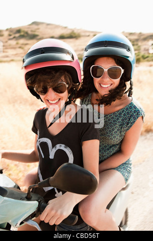 Smiling women riding scooter together Stock Photo