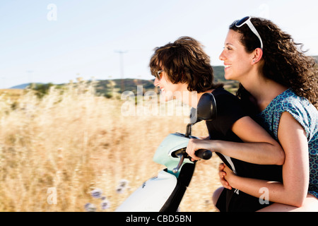 Smiling women riding scooter together Stock Photo