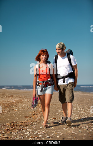 happy, young couple walking together on a deserted beach, wearing backpacks, talking  Stock Photo