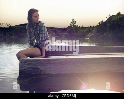 Woman sitting on dock by lake Stock Photo