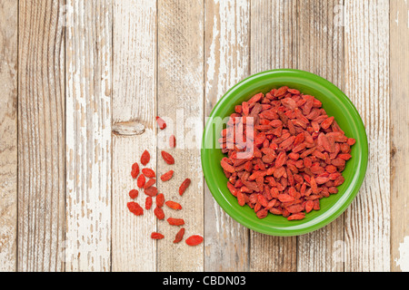 dried Tibetan goji berries (wolfberries) in a green ceramic bowl on a grunge white painted wood surface Stock Photo