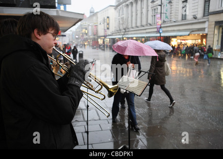 Buskers play xmas carols while people with umbrellas walk past in heavy rain Northumberland St, Newcastle. Stock Photo
