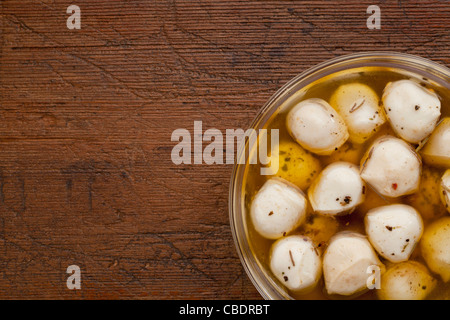 balls of mozzarella cheese marinated in oil with seasoning, glass bowl on weathered wood background Stock Photo