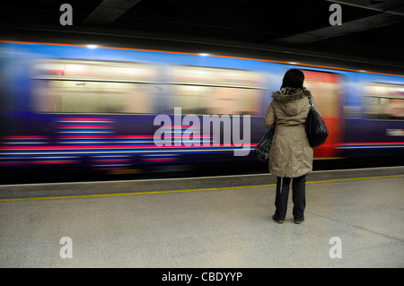 Back view lone woman passenger standing alone on station platform moving Thameslink train departing St Pancras station (low level) London England UK Stock Photo