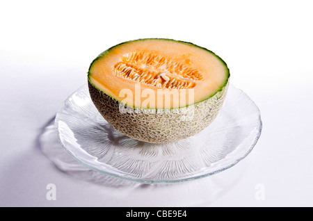 Half a cantaloupe, cut open, seeds inside, sitting on a glass plate. Stock Photo