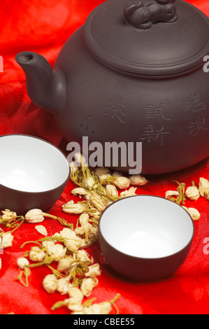 jasmine tea dry flowers,pot and two cups ,over red silk tablecloth Stock Photo