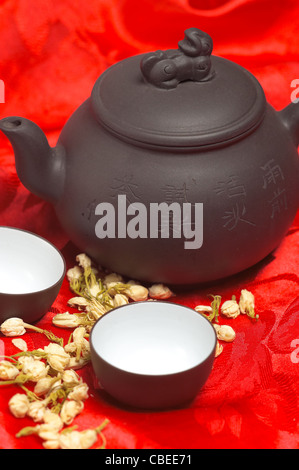 jasmine tea dry flowers,pot and two cups ,over red silk tablecloth Stock Photo