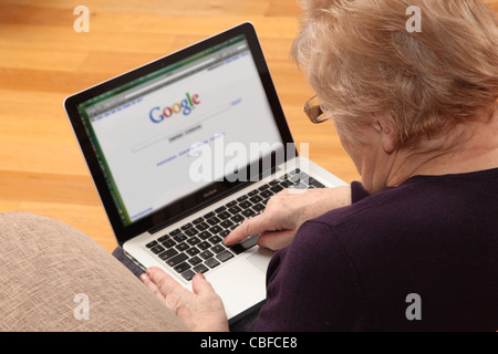 Mature woman using her laptop, on the internet with search engine on screen. Stock Photo