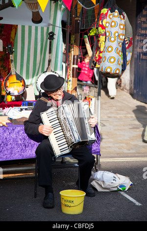 Louth Victorian Market,  Lincolnshire, England old musician man playing accordion in bowler hat with bucket for tips Stock Photo