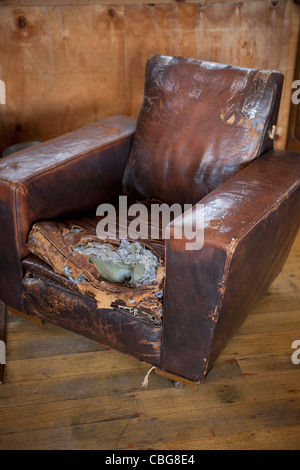 An old weathered leather armchair with torn cushion Stock Photo