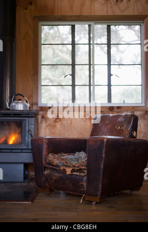 A well worn leather armchair next to a wood burning stove Stock Photo