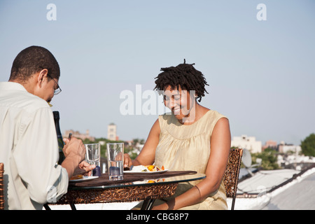 Over the shoulder view of a couple eating a meal on a rooftop terrace Stock Photo