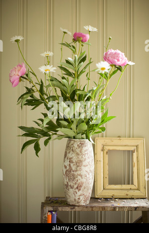 A vase of peonies and daisies and an empty picture frame Stock Photo