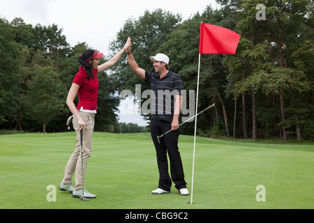 A female golfer high-fiving a male golfer on the putting green Stock Photo