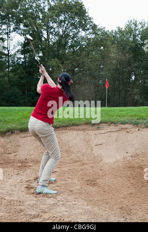 A female golfer hitting a ball out of a sand trap Stock Photo