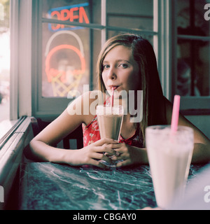 A teenage girl drinking a milkshake in a diner Stock Photo