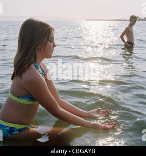 A teenage girl scooping on water while wading in the sea Stock Photo
