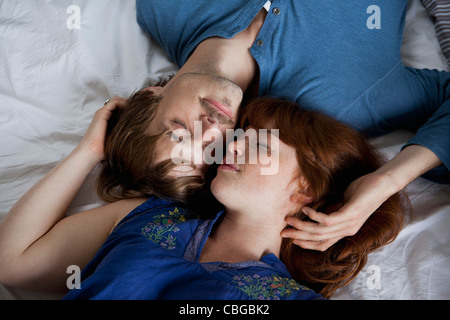 A young couple lying head to head on a bed, eyes closed Stock Photo