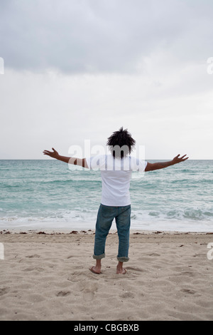 A young man standing on beach with arms outstretched, rear view Stock Photo