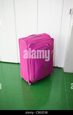 Pink suitcase contrasted against green floor and white door Stock Photo