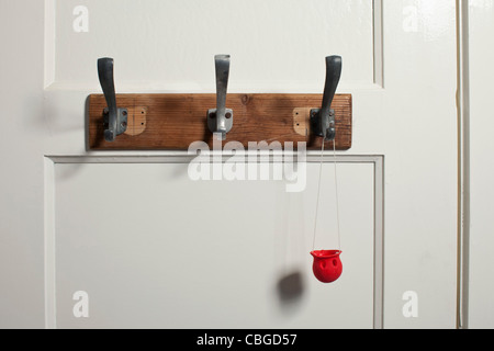 Red clown's nose hanging from coat hook on door Stock Photo