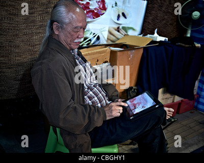 Elderly Asian man using an iPad tablet to play games. Thailand S. E. Asia Stock Photo