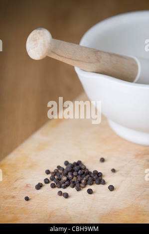 a porcelain pestle and mortar with black peppercorns on a wooden chopping board Stock Photo