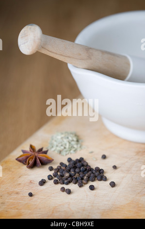 a porcelain pestle and mortar with black peppercorns, star anise and fennel seeds on a wooden chopping board Stock Photo