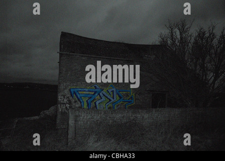 Black and white view of a barn with graffiti in colour on the side of the barn with noise added in Photoshop CS5 Stock Photo