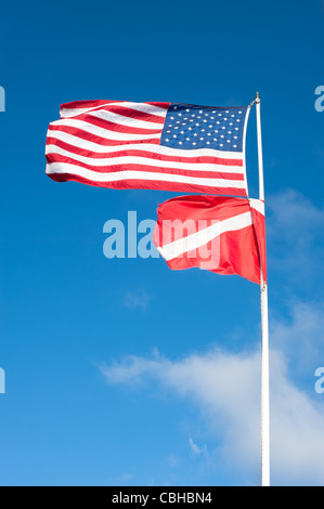 American flag and international scuba flag blowing in strong wind against a blue sky. Stock Photo