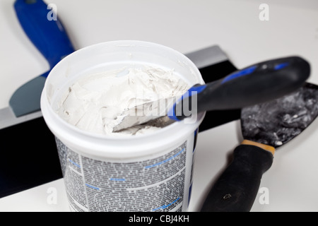Knife in patching plaster in plastic tube with other tools on the floor Stock Photo