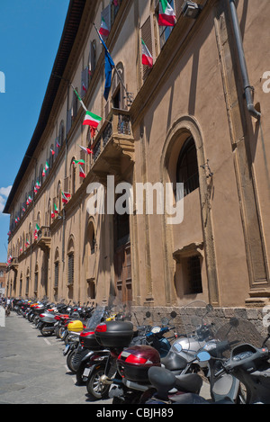 A row of parked motorscooters and motorcycles in a line along the front of a long building in Siena, Italy. Stock Photo