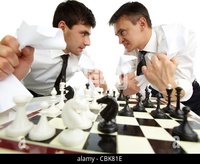 Two men with papers looking at each other aggressively while playing chess Stock Photo