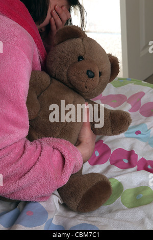Girl wearing a pink dressing gown, wiping tears from her eyes, holding a teddy bear. Stock Photo