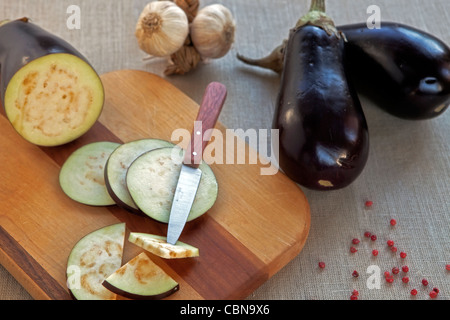 Eggplant, whole and cut, with knife on a wooden board  Stock Photo