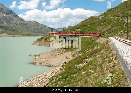 Alpine train in a mountain landscape at Lago Bianco, Bernina Pass, Grisons, Switzerland in summer Stock Photo